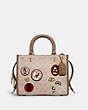 COACH®,DISNEY X COACH ROGUE BAG 25 IN SIGNATURE CANVAS WITH PATCHES,Signature Coated Canvas/Smooth Leather,Medium,Brass/Sand Taupe,Front View