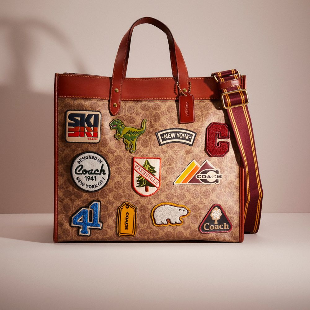 COACH®,RESTORED FIELD TOTE 40 IN SIGNATURE CANVAS WITH PATCHES,Signature Coated Canvas,Large,Brass/Tan,Front View